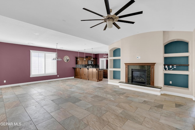 unfurnished living room featuring ceiling fan, vaulted ceiling, built in features, and a premium fireplace