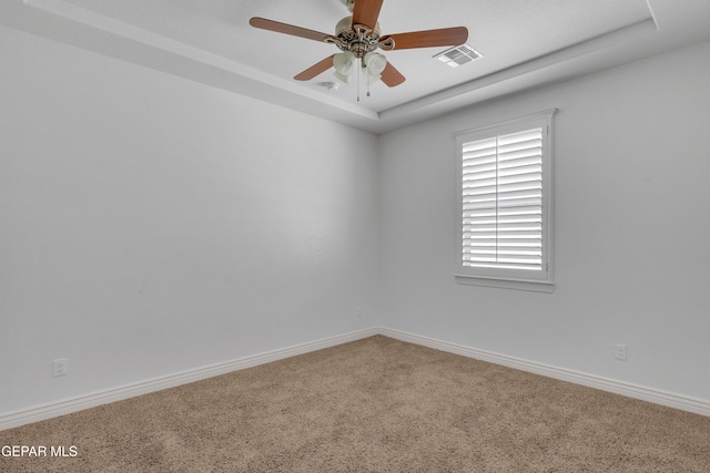 carpeted spare room with a raised ceiling and ceiling fan