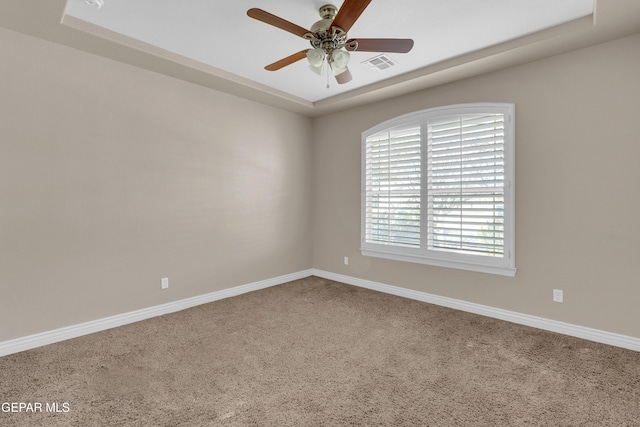 carpeted spare room featuring a tray ceiling and ceiling fan