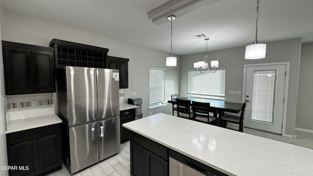 kitchen with tasteful backsplash, hanging light fixtures, stainless steel refrigerator, and a chandelier