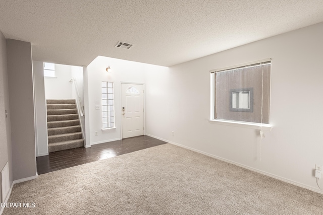 foyer entrance with dark carpet and a textured ceiling