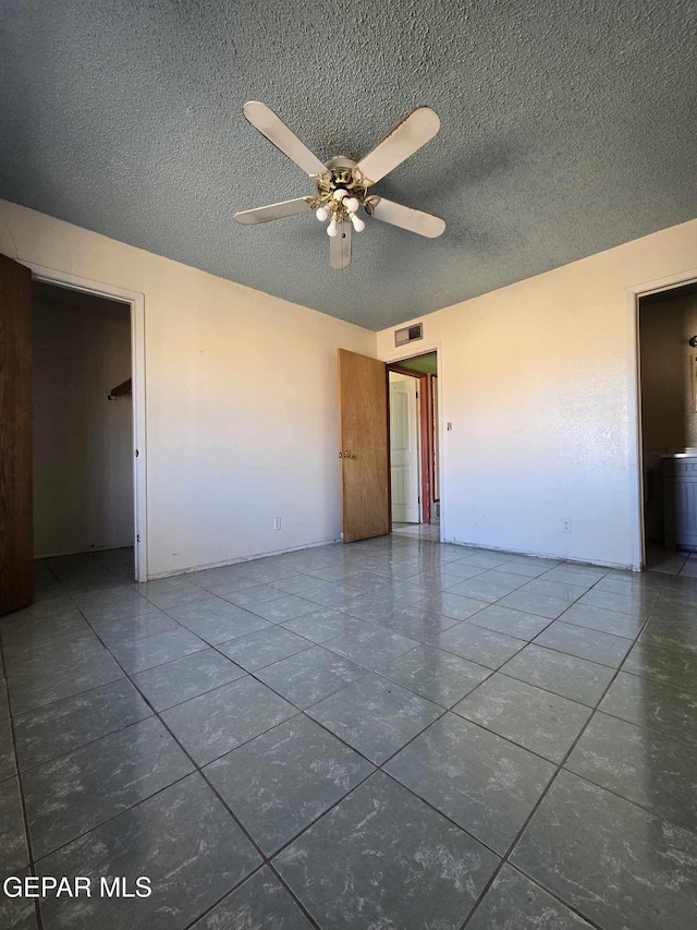 unfurnished room with ceiling fan, dark tile patterned floors, and a textured ceiling