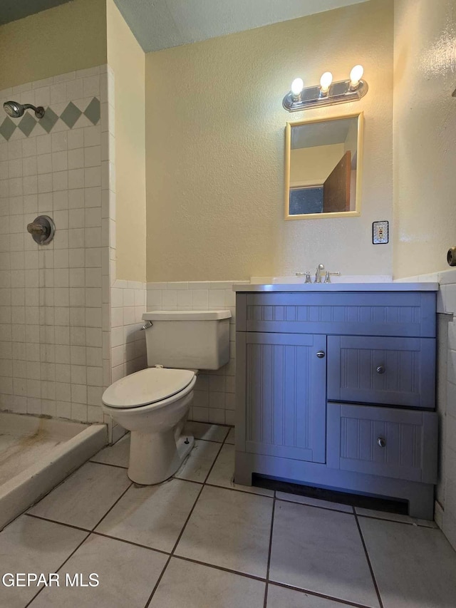 bathroom with tiled shower, tile patterned flooring, vanity, and toilet