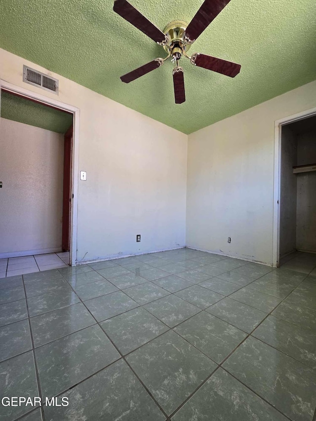 interior space featuring a textured ceiling, dark tile patterned flooring, and ceiling fan