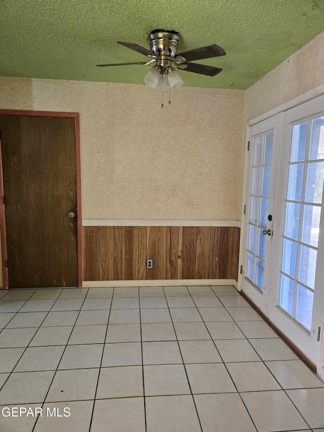 spare room featuring ceiling fan, a textured ceiling, wooden walls, and french doors