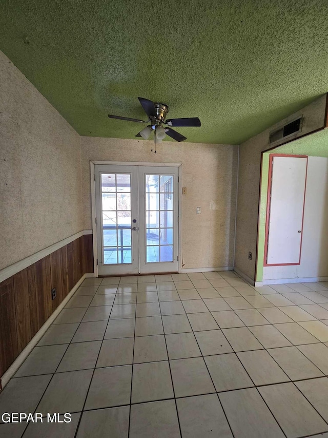 tiled spare room featuring french doors, a textured ceiling, ceiling fan, and wood walls