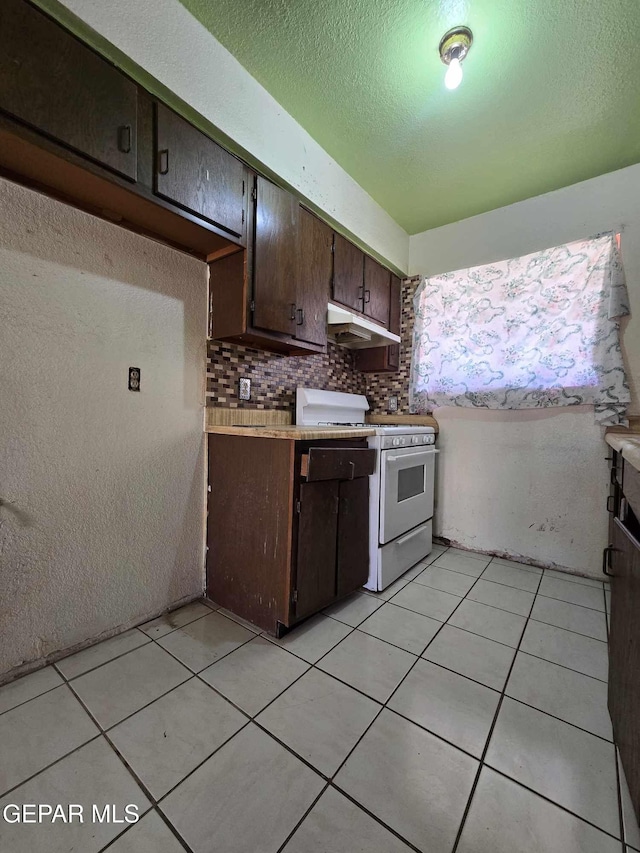 kitchen with a textured ceiling, dark brown cabinetry, white gas range oven, and tasteful backsplash