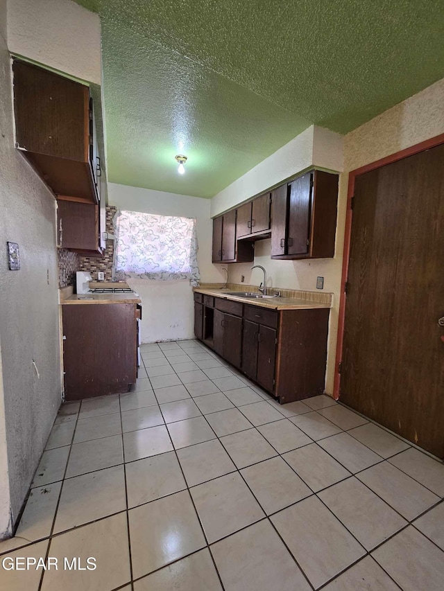 kitchen featuring dark brown cabinetry, sink, range with gas cooktop, a textured ceiling, and light tile patterned flooring