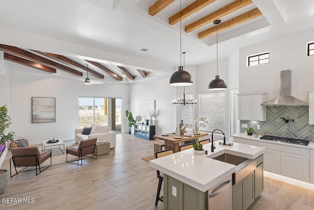 kitchen featuring tasteful backsplash, stainless steel appliances, a kitchen island with sink, wall chimney range hood, and pendant lighting