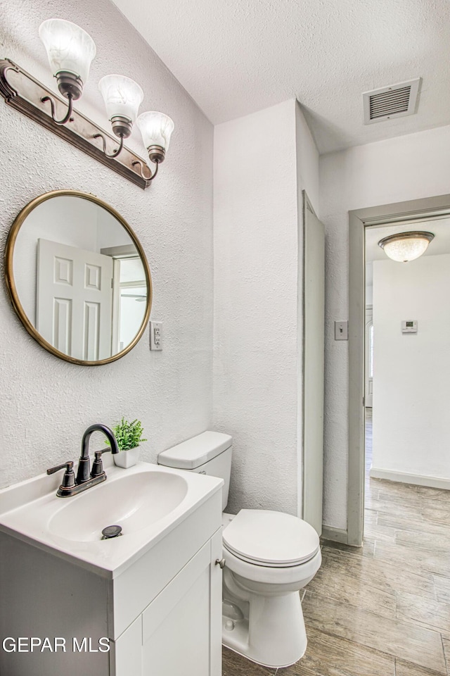 bathroom featuring vanity, wood-type flooring, a textured ceiling, and toilet