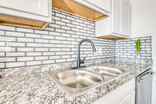 kitchen with light stone counters, sink, white cabinets, and stainless steel dishwasher