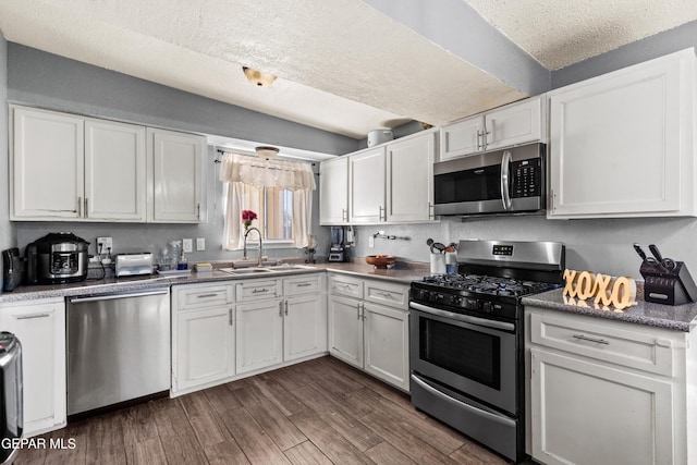 kitchen with appliances with stainless steel finishes, a textured ceiling, dark hardwood / wood-style floors, white cabinets, and sink