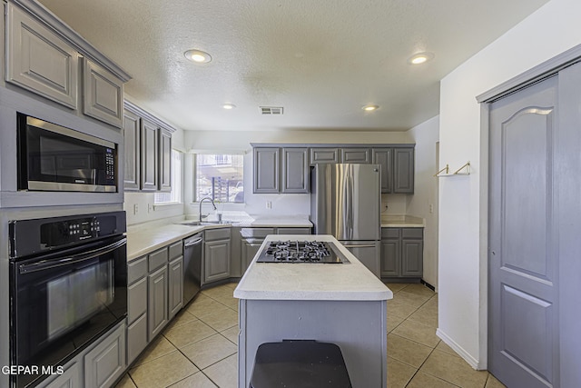 kitchen with appliances with stainless steel finishes, gray cabinetry, light tile patterned floors, a kitchen island, and sink