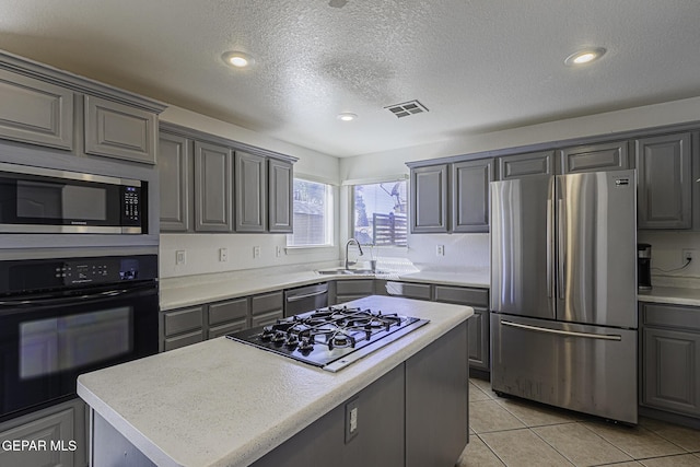 kitchen with stainless steel appliances, sink, a textured ceiling, light tile patterned floors, and a kitchen island