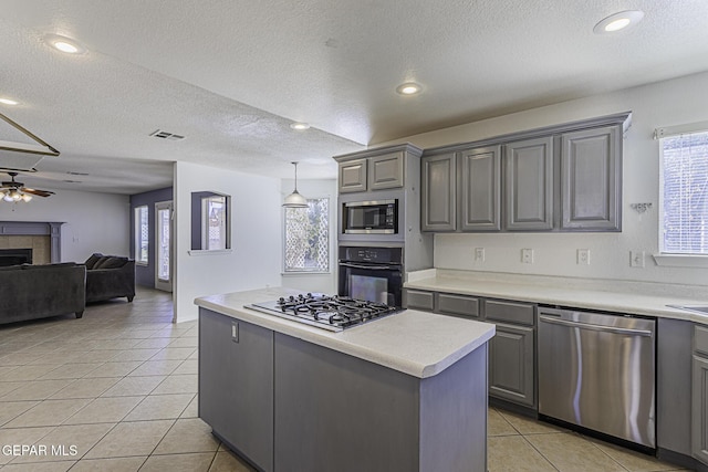 kitchen with stainless steel appliances, a tile fireplace, light tile patterned floors, gray cabinets, and a kitchen island