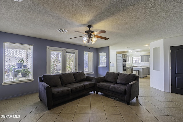 living room with a textured ceiling, ceiling fan, and light tile patterned floors