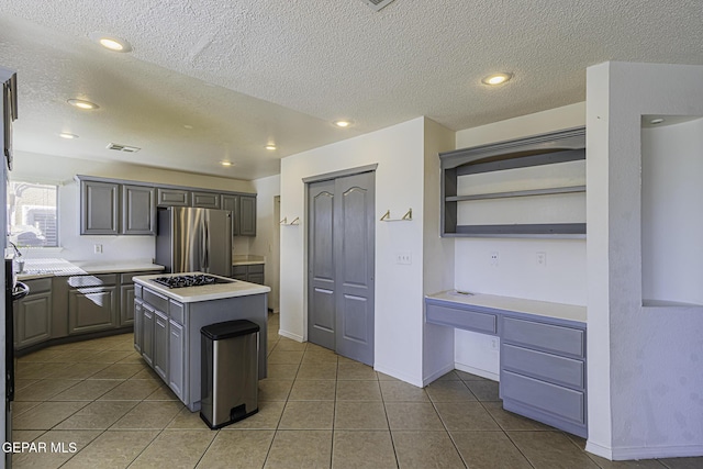 kitchen featuring a kitchen island, black gas cooktop, gray cabinets, tile patterned floors, and stainless steel refrigerator