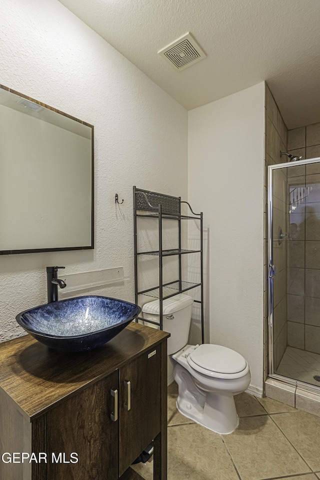 bathroom featuring toilet, a textured ceiling, a shower with door, tile patterned floors, and vanity