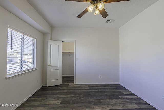 unfurnished bedroom featuring a closet, ceiling fan, dark hardwood / wood-style flooring, a spacious closet, and a textured ceiling