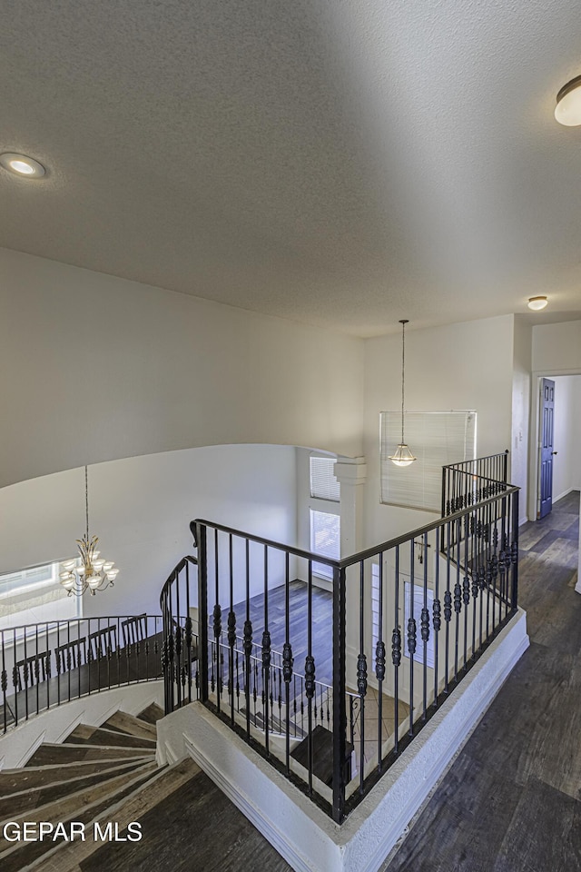 staircase with hardwood / wood-style flooring, an inviting chandelier, and a textured ceiling