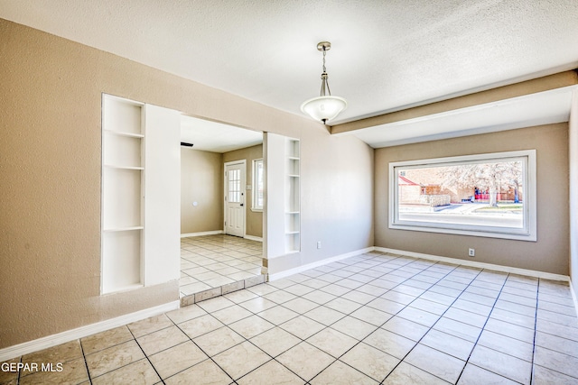 empty room with built in features, light tile patterned flooring, and a textured ceiling