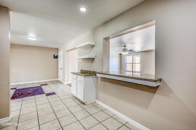 kitchen featuring white cabinets, kitchen peninsula, ceiling fan, and dark stone counters