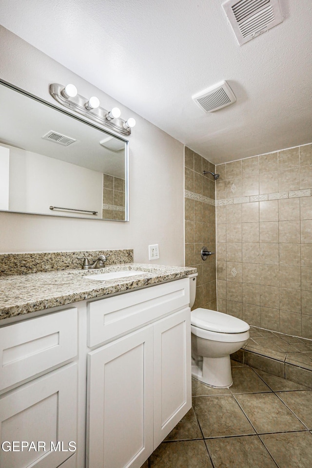 bathroom featuring tile patterned floors, a textured ceiling, vanity, tiled shower, and toilet