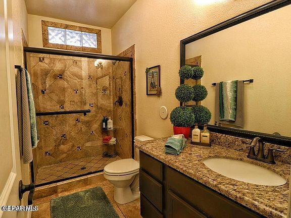 bathroom featuring tile patterned flooring, vanity, a shower with shower door, and toilet