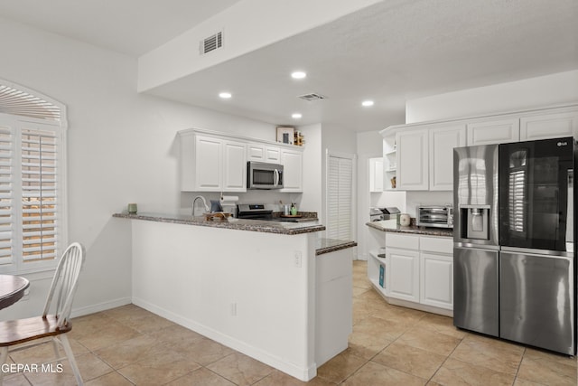 kitchen with appliances with stainless steel finishes, dark stone counters, white cabinets, and kitchen peninsula