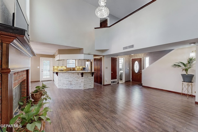 entryway with a high ceiling, dark hardwood / wood-style flooring, an inviting chandelier, and a brick fireplace