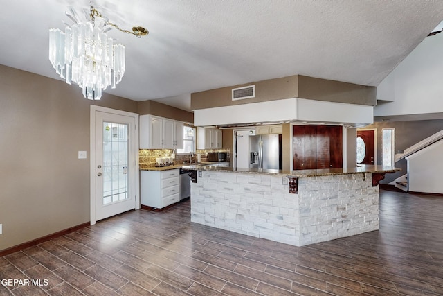 kitchen with white cabinetry, backsplash, hanging light fixtures, stainless steel fridge, and a chandelier