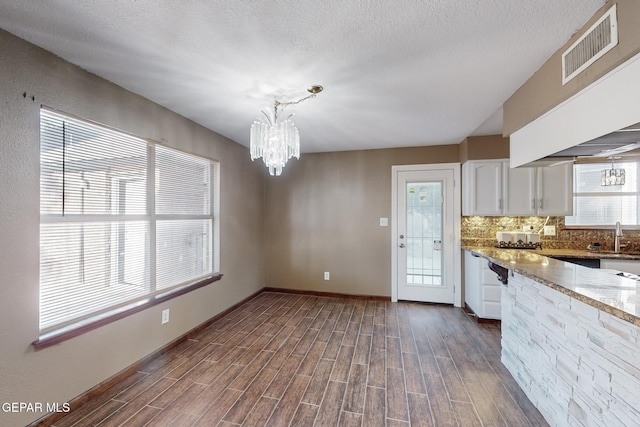 kitchen with light stone countertops, a chandelier, pendant lighting, decorative backsplash, and white cabinetry