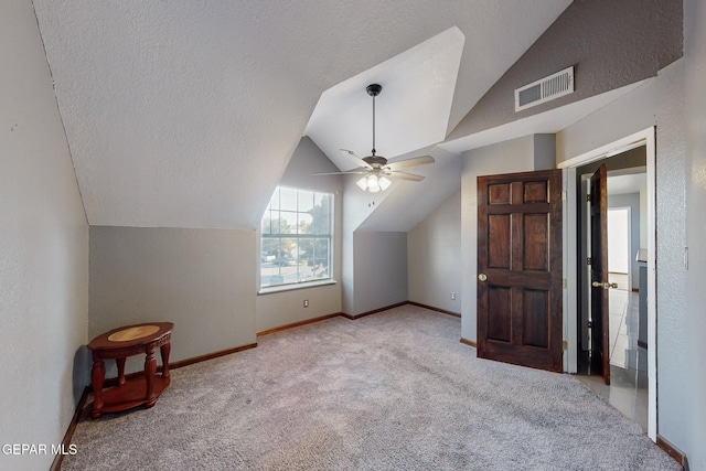 additional living space with lofted ceiling, a textured ceiling, light colored carpet, and ceiling fan