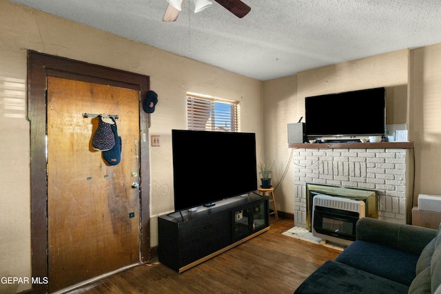 living room with ceiling fan, dark wood-type flooring, a textured ceiling, and a fireplace