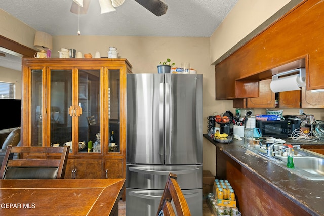 kitchen with stainless steel fridge, ceiling fan, dark stone counters, a textured ceiling, and sink