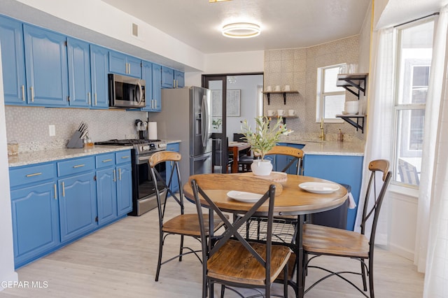 kitchen with stainless steel appliances, blue cabinets, tasteful backsplash, light hardwood / wood-style flooring, and light stone countertops