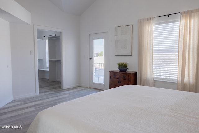 bedroom featuring light hardwood / wood-style floors, ensuite bath, lofted ceiling, and access to exterior