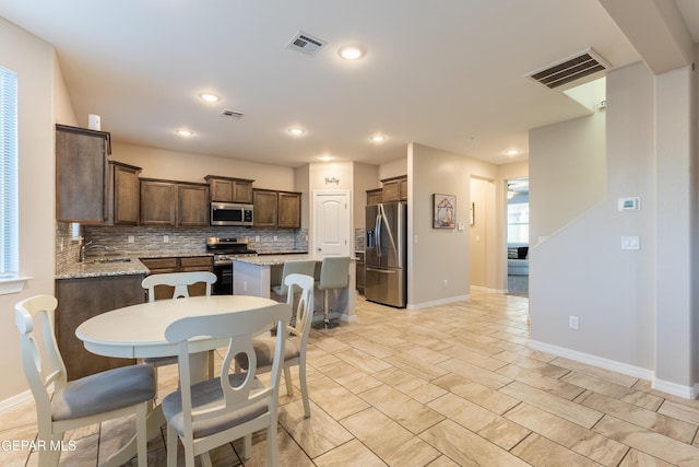 kitchen featuring light stone countertops, appliances with stainless steel finishes, tasteful backsplash, sink, and a center island