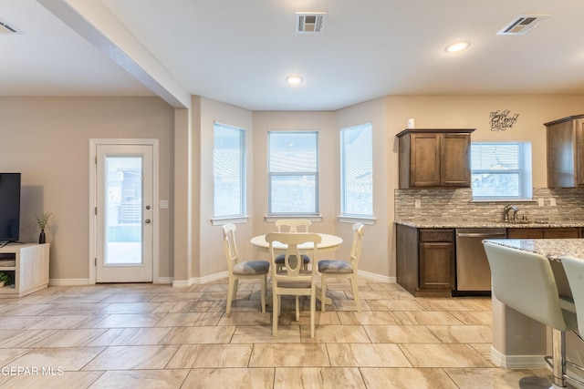 kitchen featuring backsplash, light stone counters, plenty of natural light, and stainless steel dishwasher