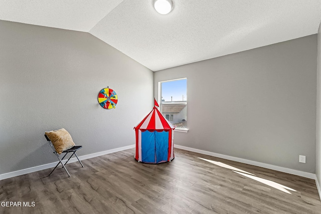 game room featuring vaulted ceiling, hardwood / wood-style floors, and a textured ceiling