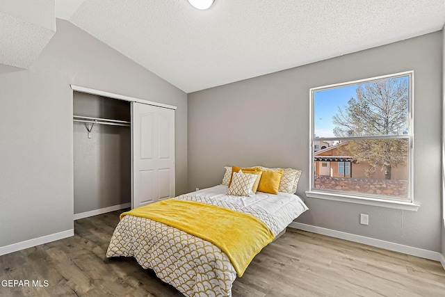 bedroom with wood-type flooring, vaulted ceiling, a closet, and a textured ceiling