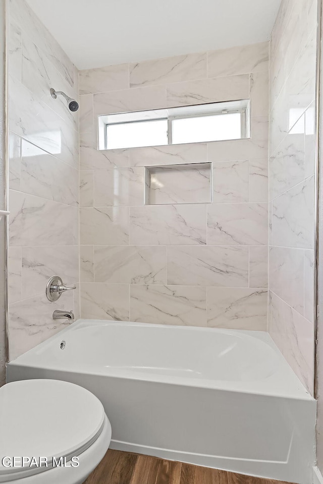 bathroom with hardwood / wood-style floors, toilet, and tiled shower / bath