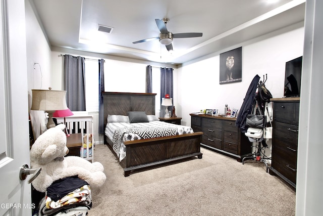 bedroom featuring light carpet, ceiling fan, and a tray ceiling