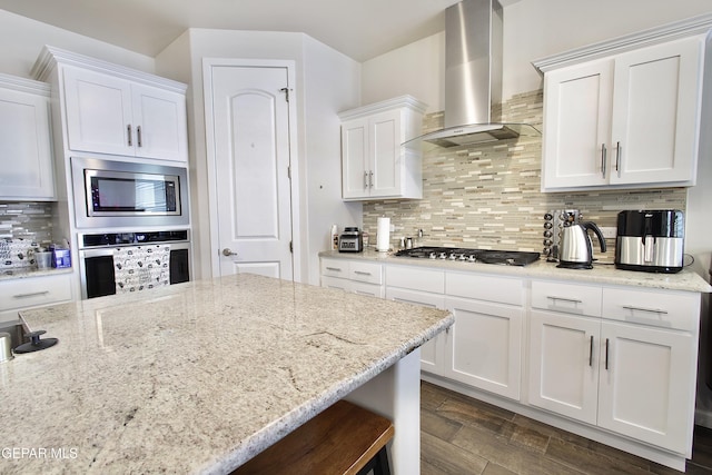 kitchen featuring appliances with stainless steel finishes, white cabinetry, wall chimney range hood, and backsplash