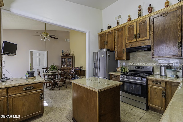 kitchen with ceiling fan, appliances with stainless steel finishes, tasteful backsplash, light stone countertops, and a kitchen island