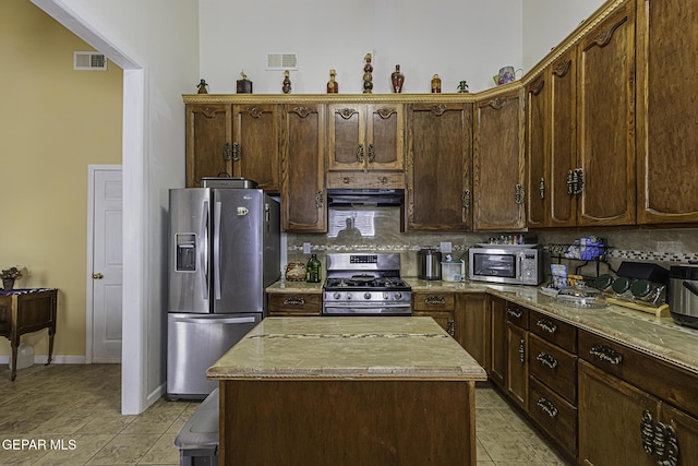 kitchen with appliances with stainless steel finishes, decorative backsplash, light stone counters, and a center island