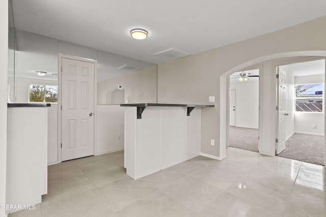 kitchen with arched walkways, a breakfast bar, a ceiling fan, white cabinets, and dark countertops