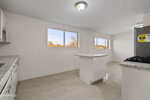 kitchen featuring tasteful backsplash, white cabinetry, a textured ceiling, light stone countertops, and stainless steel fridge