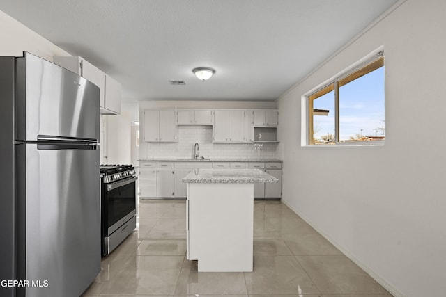 kitchen with tasteful backsplash, appliances with stainless steel finishes, white cabinets, a sink, and a kitchen island