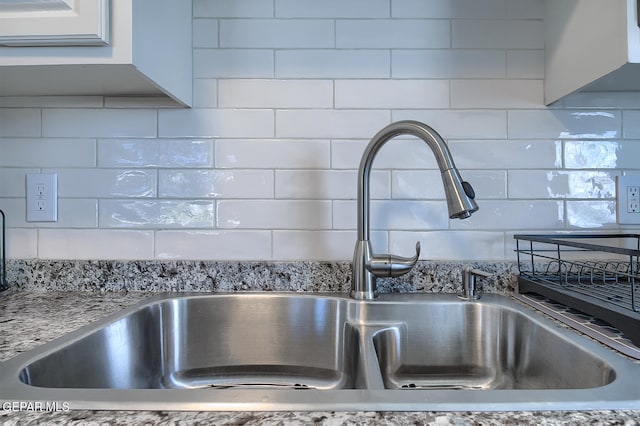 interior details featuring sink, light stone counters, and decorative backsplash